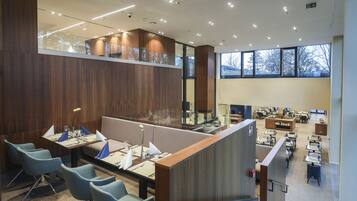 A modern dining area with high tables, comfortable seating, and large windows providing natural light.