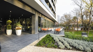 A modern building with a glass facade, outdoor seating area with tables and chairs, and landscaped garden beds. - Hunguest Hotel Sóstó (Nyiregyhaza)