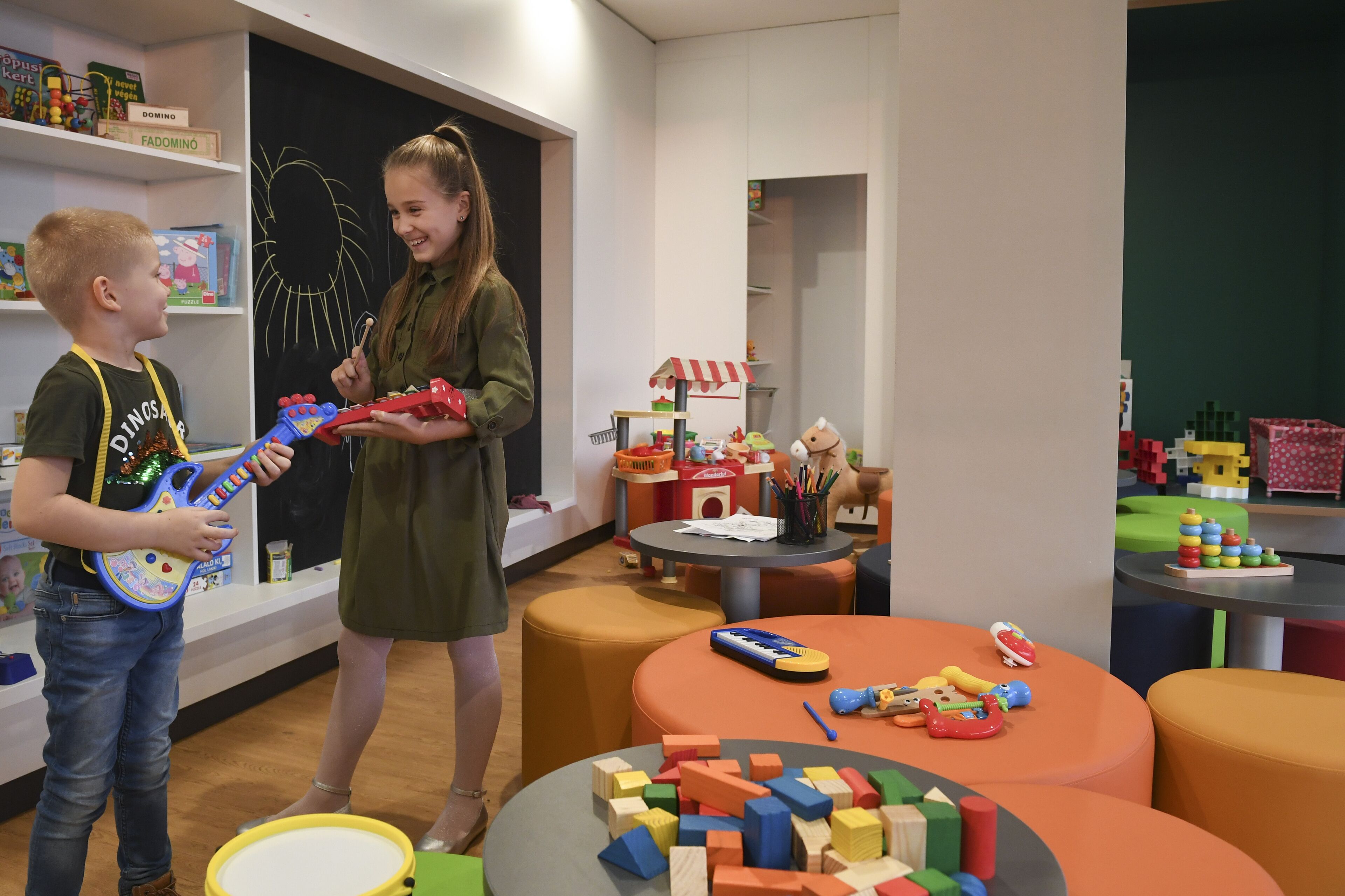 Un niño juega con una guitarra de juguete en una habitación con muebles coloridos y diversos juguetes.