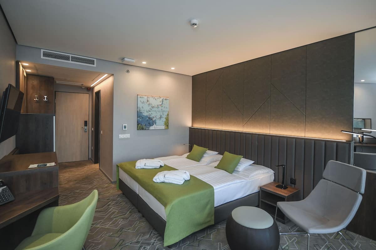 A modern hotel room with a large bed, a desk, a chair, and a small table.
