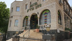 A building with a sign reading "HOTEL" and "HOTEL" in another language. It has a stone facade, arched windows, and a staircase leading to the entrance. - Bergik Hotel (Tiberias)