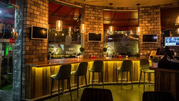 A bar area with a brick wall, bar stools, and hanging pendant lights. - Bergik Hotel (Tiberias)