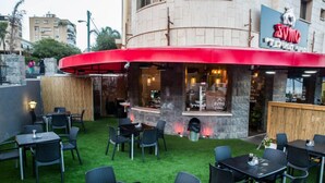 An outdoor seating area with tables and chairs, a red awning, and a stone wall. - Bergik Hotel (Tiberias)