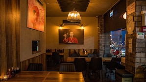 A restaurant interior with wooden tables and chairs, a large painting on the wall, and a view of the city through the window. - Bergik Hotel (Tiberias)
