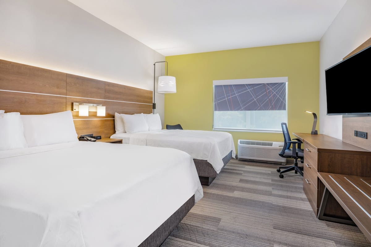 A hotel room with two beds, a desk, a chair, a TV, and a window with a view.