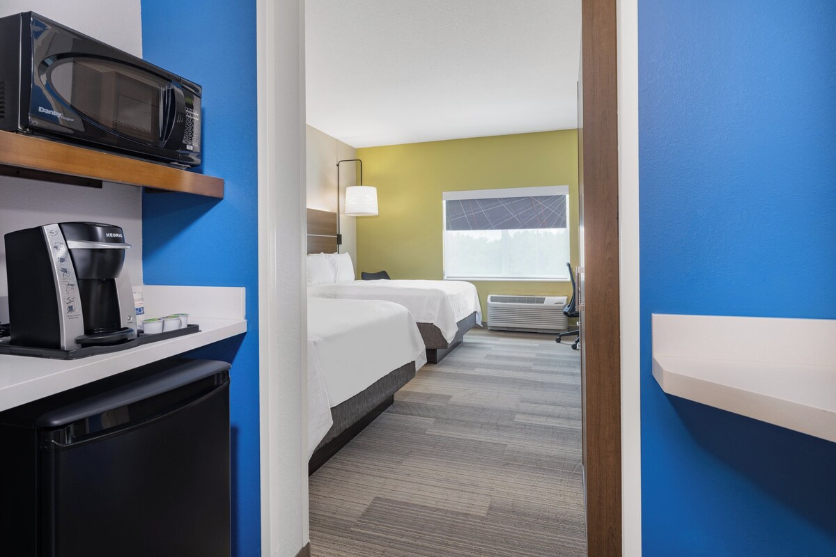Une chambre d’hôtel équipée d’une kitchenette, d’un lit, d’une fenêtre avec stores et d’une table de chevet.
