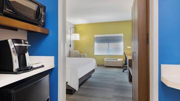 Habitación de hotel con cama, microondas, cafetera, escritorio y ventana con persianas.