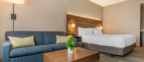 A hotel room with a sofa, a bed, a wooden coffee table, and a lamp.