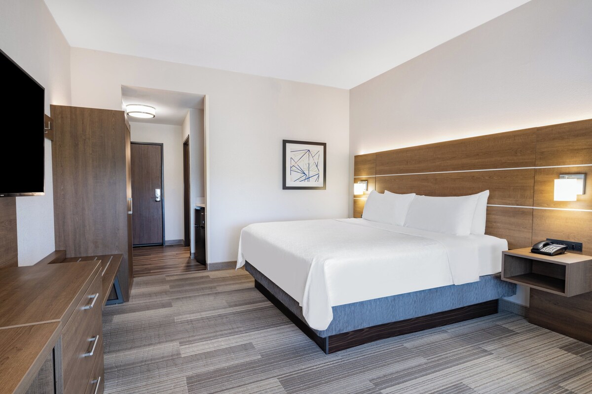 Une chambre d’hôtel moderne avec un grand lit, une tête de lit en bois, une table de chevet avec un téléphone et un téléviseur à écran plat fixé au mur.