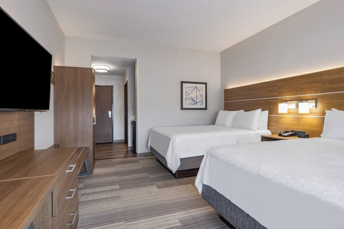 A hotel room with two beds, a TV, a desk, and a framed picture on the wall.