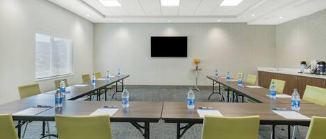 A conference room with a long table, chairs, water bottles, a TV, and a kitchenette.
