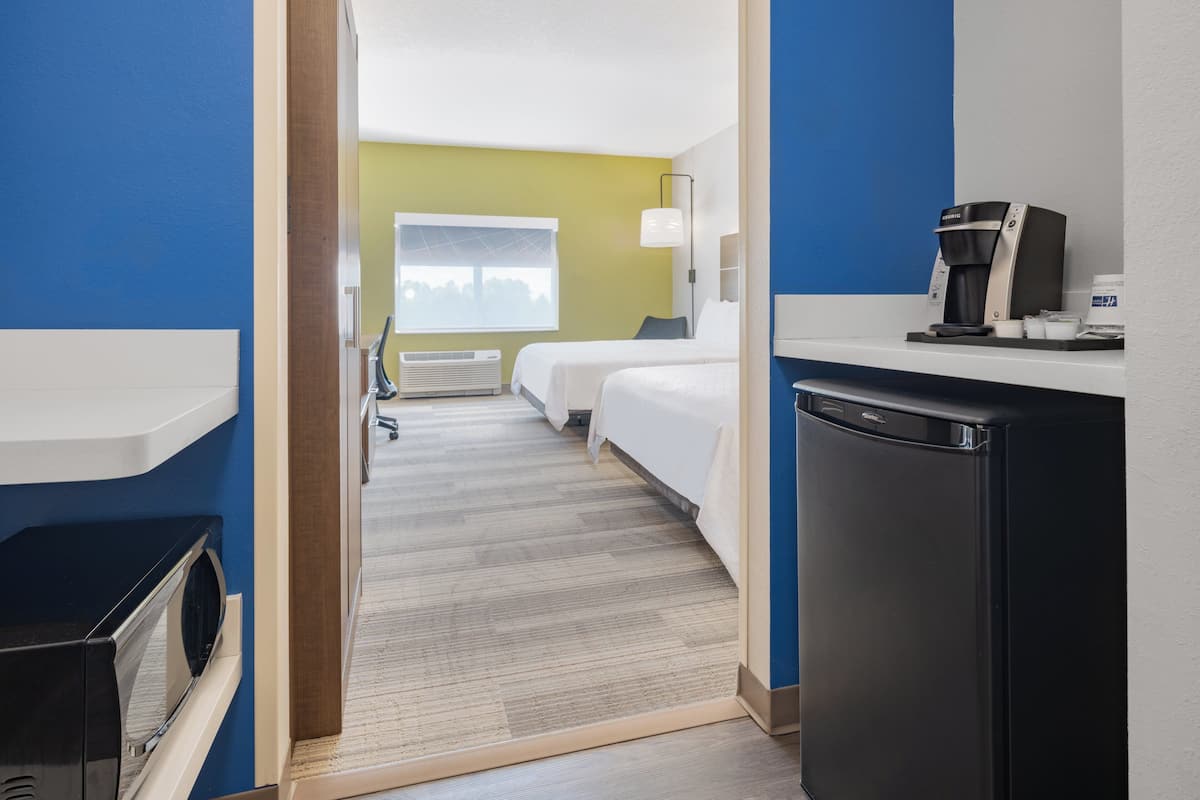 A hotel room with two beds, a kitchenette, a microwave, and a coffee maker.