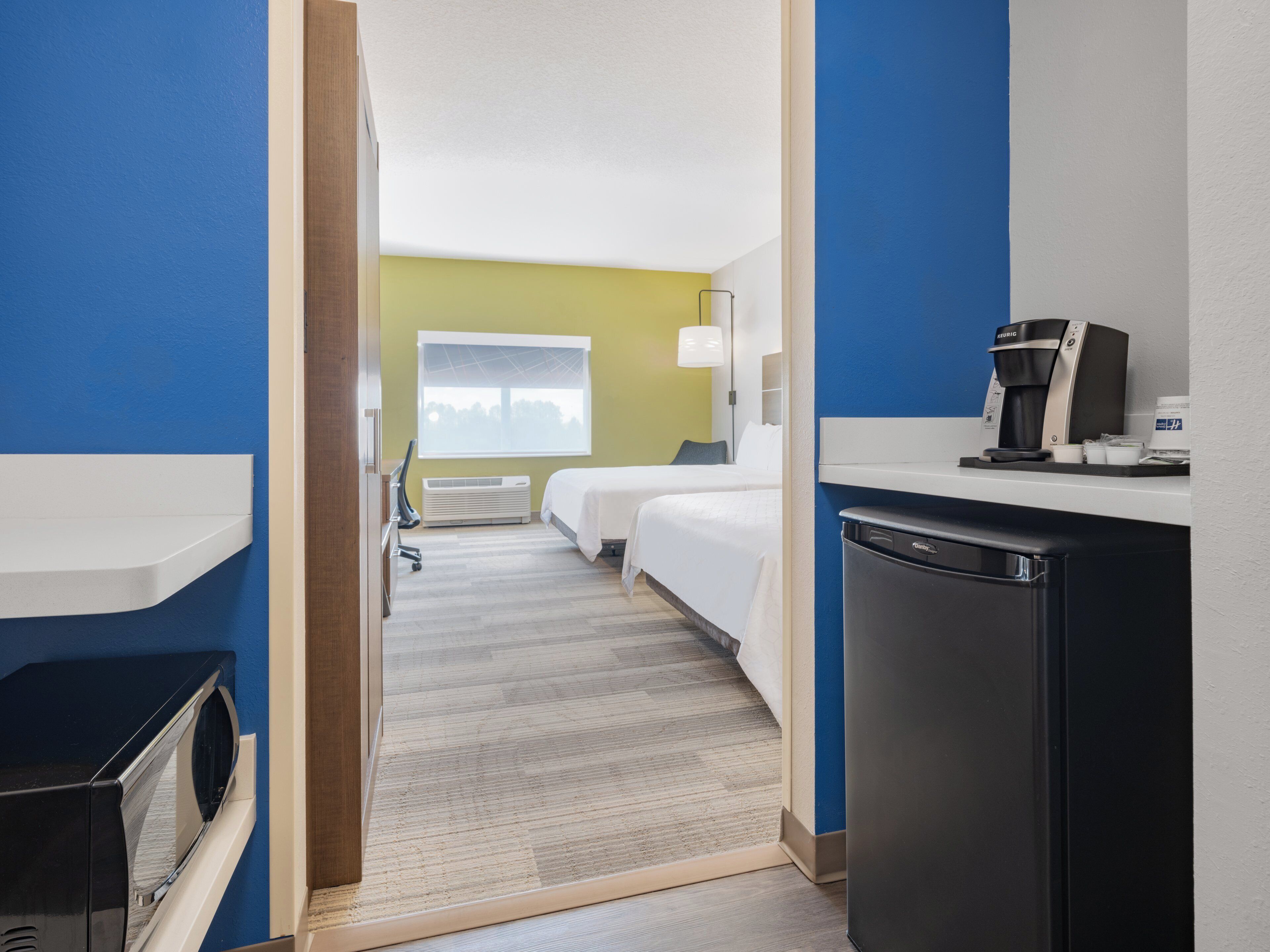 Ein Hotelzimmer mit zwei Betten, einer Küchenzeile, einer Mikrowelle und einer Kaffeemaschine.