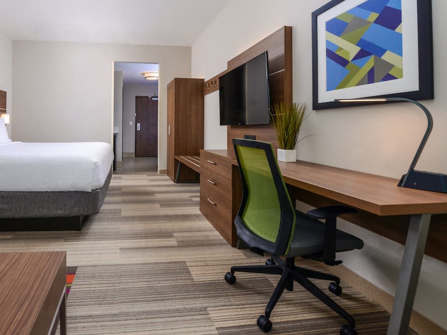 A hotel room with a bed, a desk, a chair, a television, and a framed picture on the wall.