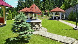 Un jardín con un pabellón de techo rojo y base de piedra, rodeado de césped cuidado y árboles.