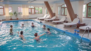 Una piscina interior con varias pistas, tumbonas y amplias ventanas con vistas al exterior.