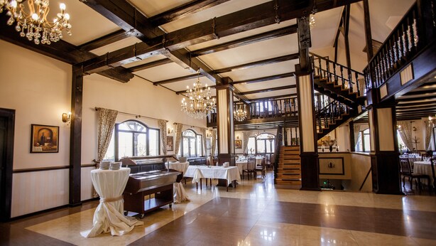 Un lobby de hotel espacioso con un piano de cola, candelabros y una escalera que lleva a un nivel superior.