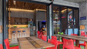 A restaurant with a wooden bar, red chairs, and a long wooden table. - Small Shells Hotel Phuket (Patong)