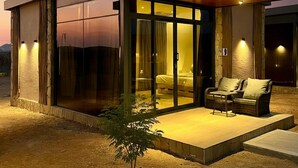 Una casa moderna con fachada de vidrio, terraza de madera y un pequeño espacio al aire libre para sentarse.
