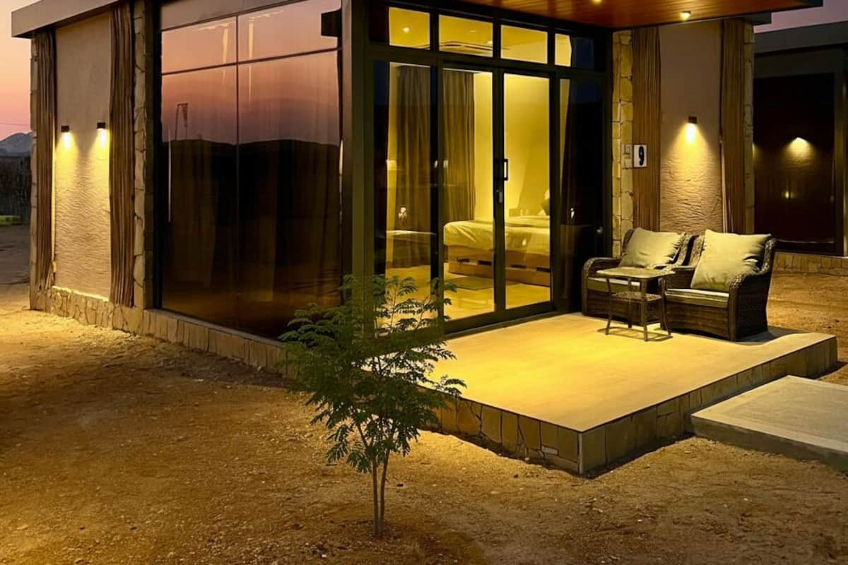 A modern house with a glass facade, a wooden deck, and a small outdoor seating area.