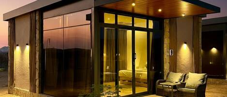 A modern house with a glass facade, a wooden deck, and a small outdoor seating area.