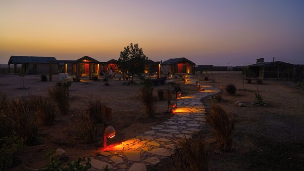 Un alojamiento de estilo desértico con varias cabañas, un sendero de piedra e iluminación exterior.