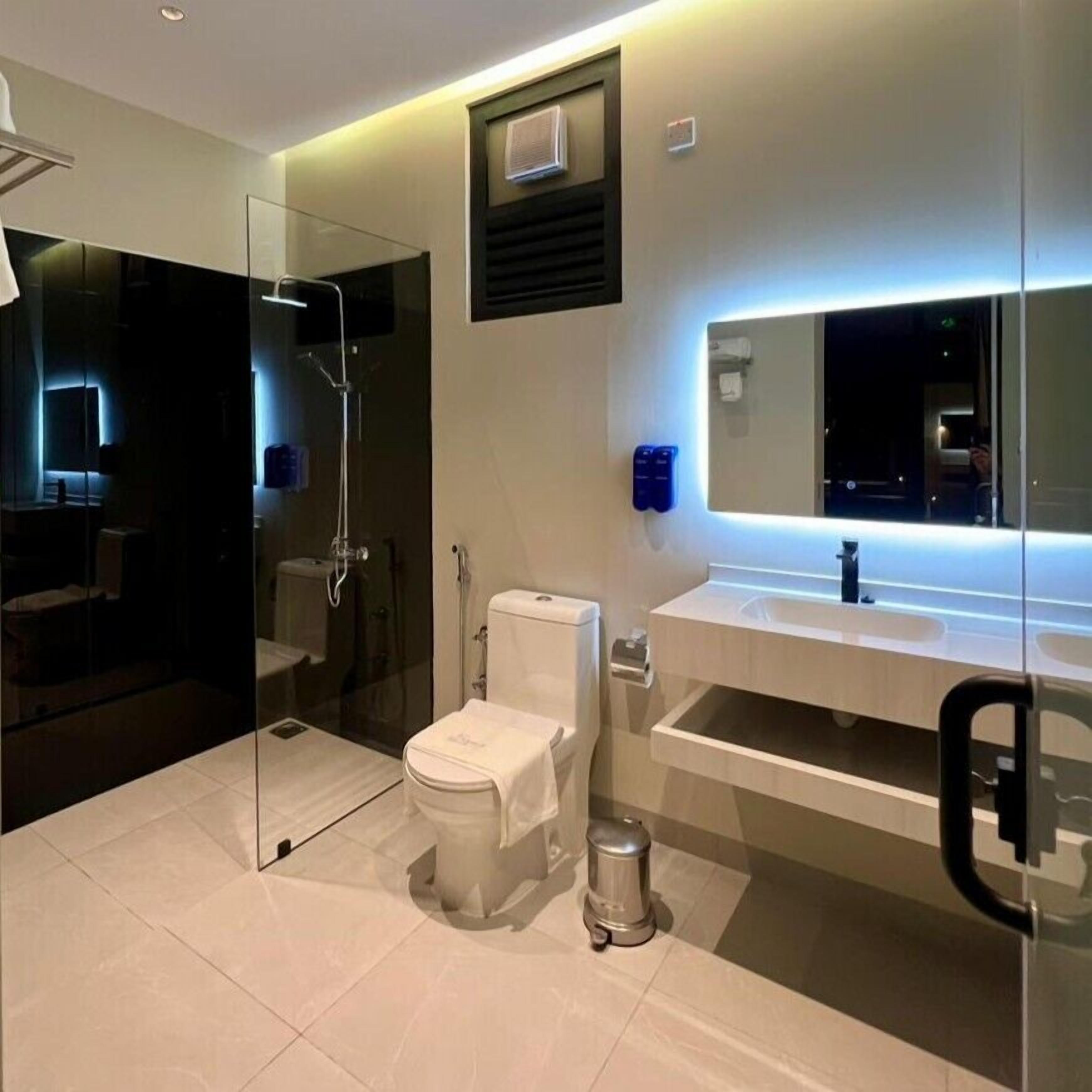 A modern bathroom with a glass-enclosed shower, a toilet, a sink with a mirror, and a trash can.