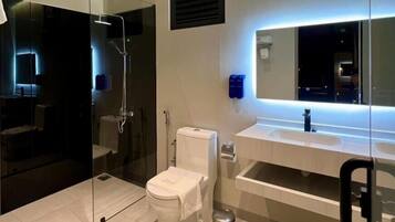 A modern bathroom with a glass-enclosed shower, a toilet, a sink with a mirror, and a trash can.
