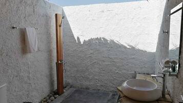 A bathroom with a stone floor, a wooden shower door, a large white basin, and a toilet.