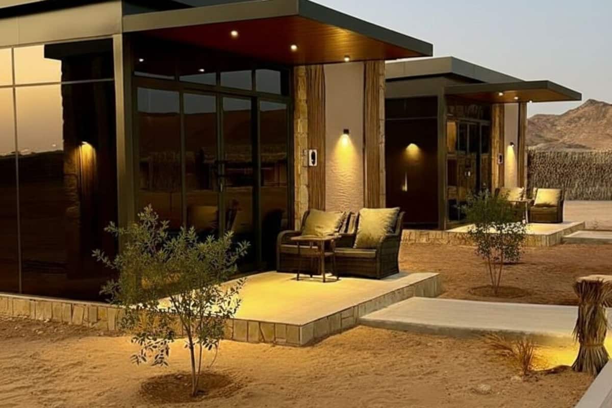 A modern building with large glass windows, outdoor seating, and a desert landscape in the background.