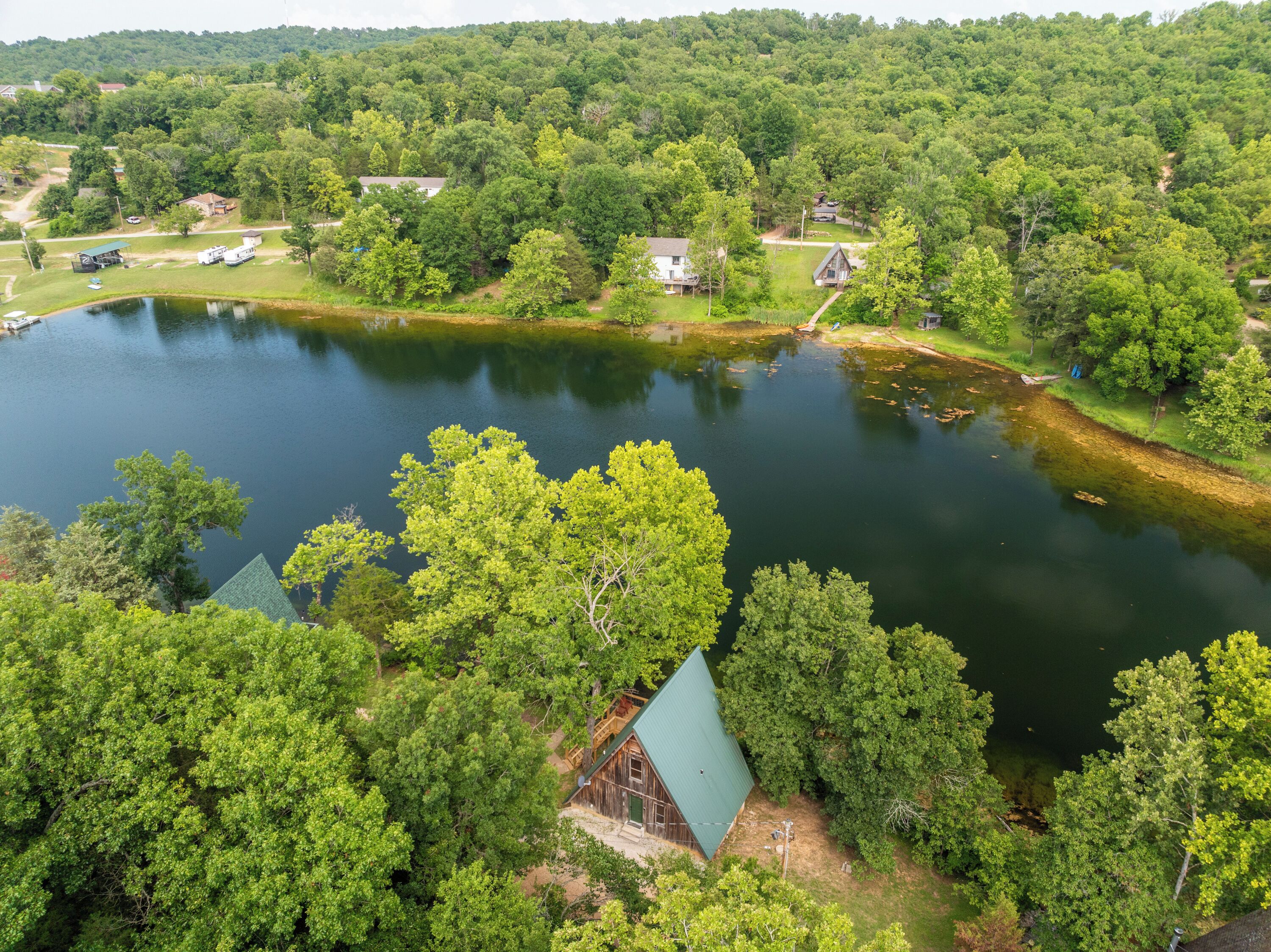 Un lago rodeado de un bosque denso y varias construcciones, incluidas cabañas y una casa.