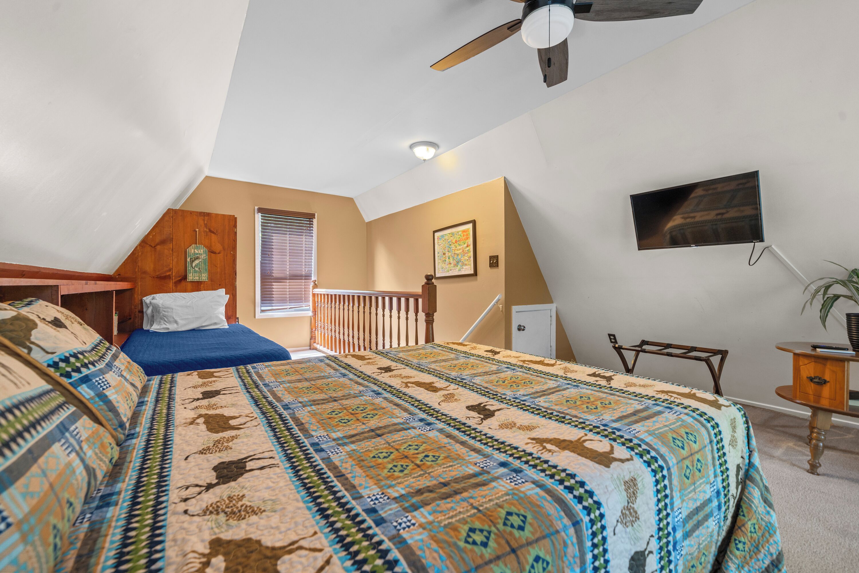 A bedroom with a large bed, a ceiling fan, a TV, and a window with blinds.