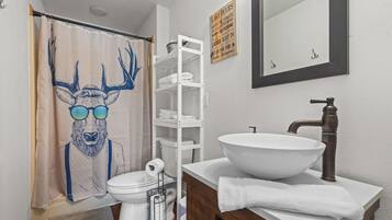 Un baño con un lavamanos blanco, un espejo, un perchero para toallas, una estantería y una cortina de ducha con un diseño de ciervo.