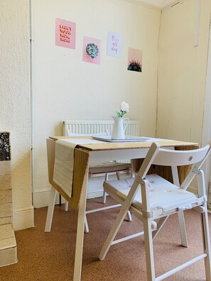 A small dining area with a white table, two white chairs, a white pitcher with a flower, and a radiator. There are three wall decorations with text. - London Walthamstow Home (London)