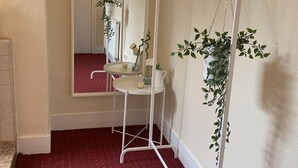 A hallway with a white metal drying rack with lights, a small round table with a vase of flowers, and a mirror on the wall. - London Walthamstow Home (London)