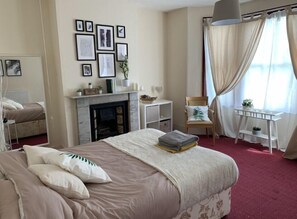 A bedroom with a bed, a fireplace, a desk, and a chair.