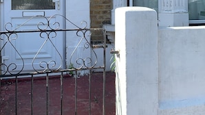 A white townhouse with a black metal gate, a brick wall, and a number '13' on the door. - London Walthamstow Home (London)