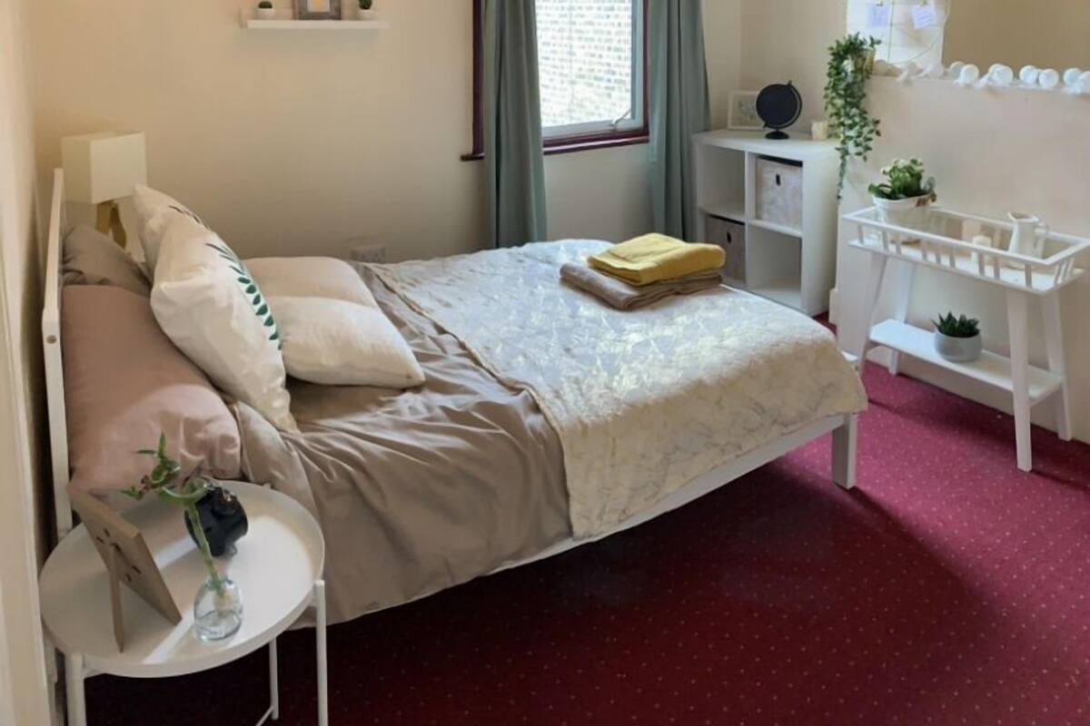 A neatly arranged bedroom with a bed, bedside table, and a small desk with a mirror.