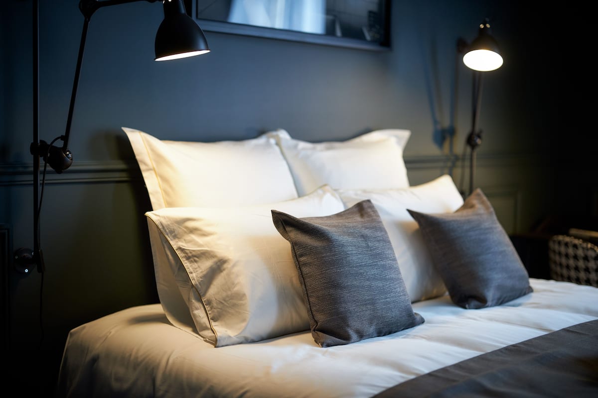 A neatly made bed with white and grey pillows, two bedside lamps, and a wall-mounted mirror above the bed.