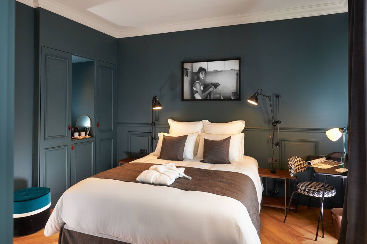 A neatly arranged bedroom with a bed, bedside tables, a desk, and a chair.