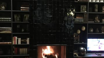 Un salon chaleureux avec une cheminée, entouré d’étagères remplies de livres et d’objets décoratifs.