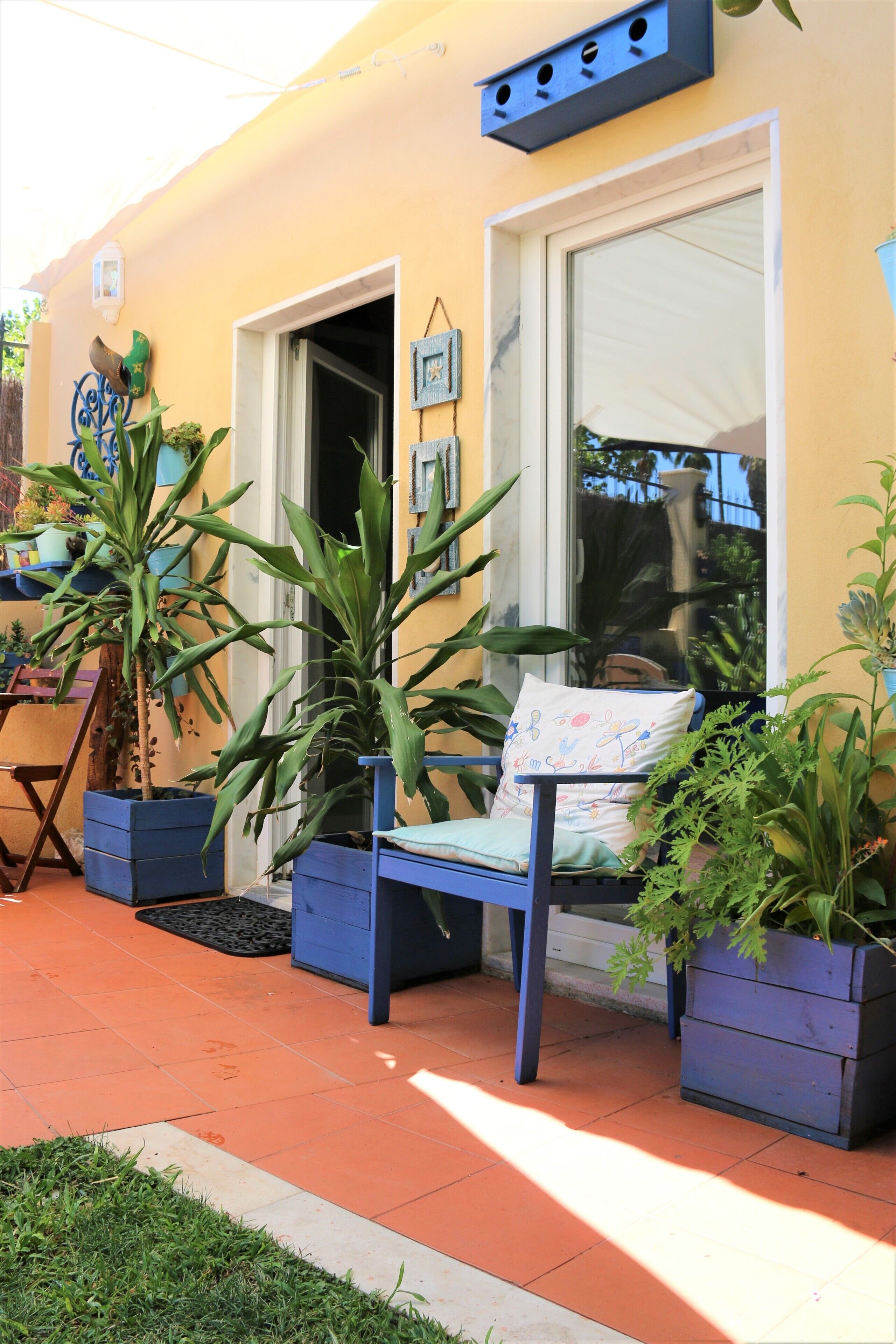 A yellow building with a blue bench and potted plants.