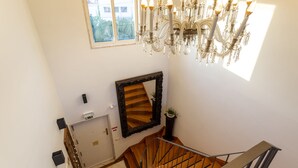 A staircase with a wooden handrail, a chandelier, a mirror, and a window with a view of buildings. - Geronimo Guest House Belém (Lisbon)