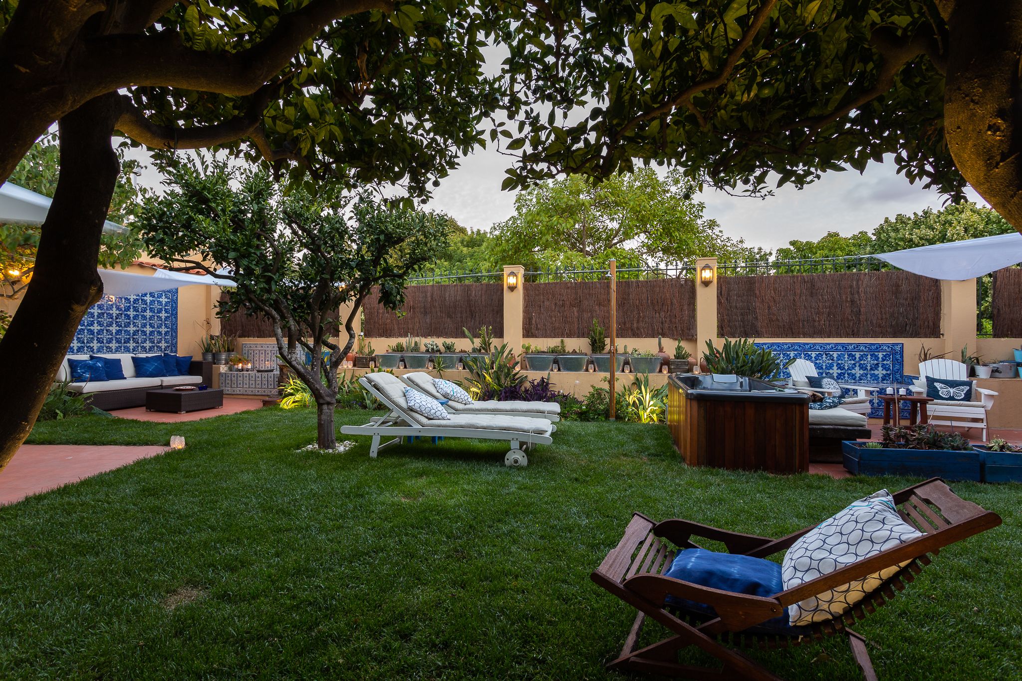 A backyard with a seating area, including a sofa and lounge chairs, surrounded by a garden and a decorative wall.