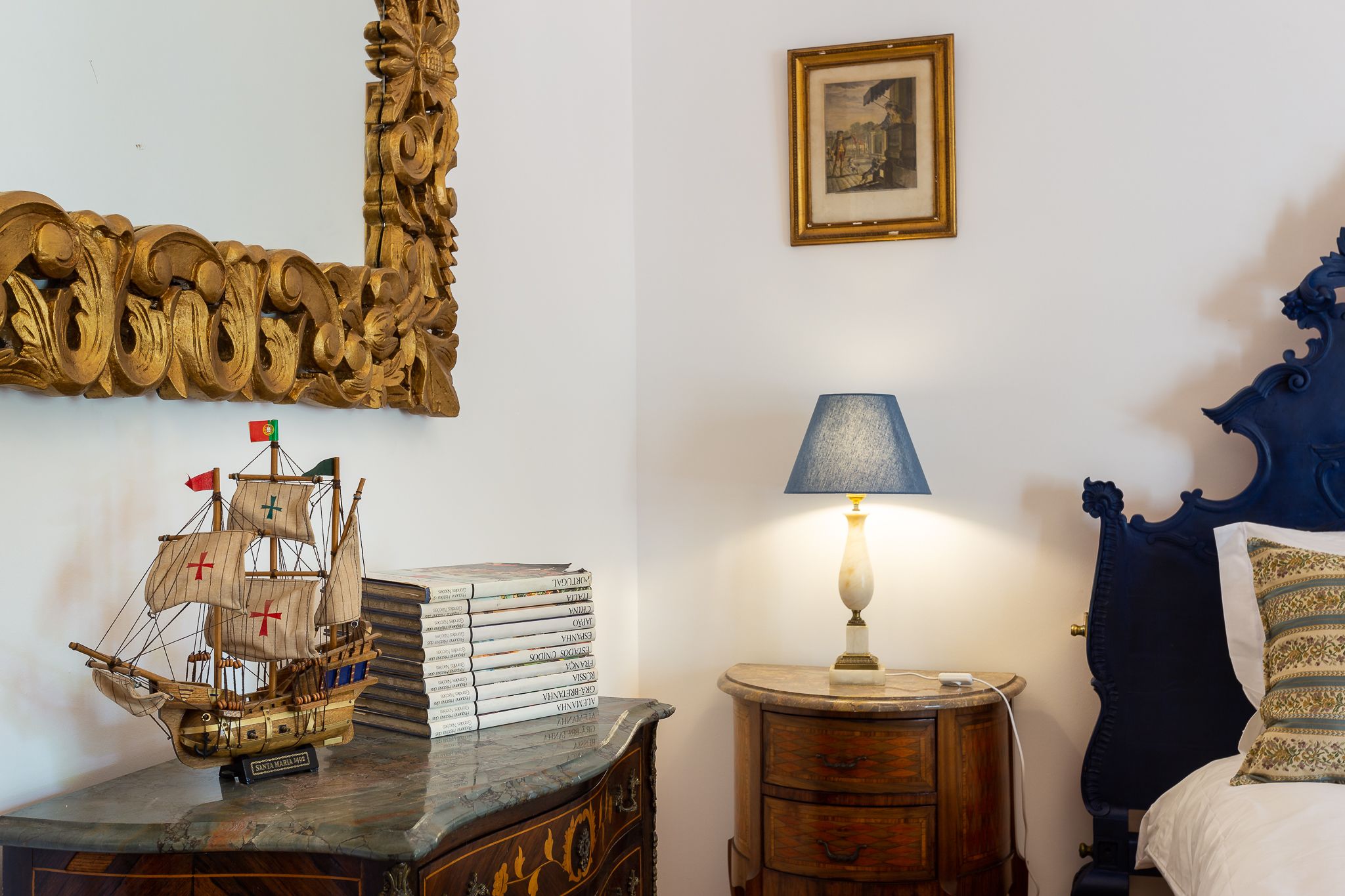 Un dormitorio con cama, mesita de noche, lámpara, cómoda de madera, espejo decorativo y un modelo de barco.