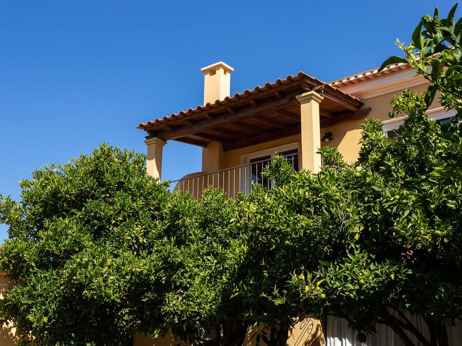 A house with a balcony, surrounded by lush green trees.