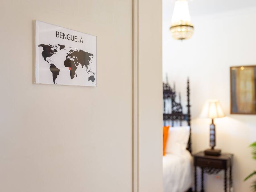 Een wereldkaart met de aanduiding 'BENGUELA', een lamp, een bed en een plant.
