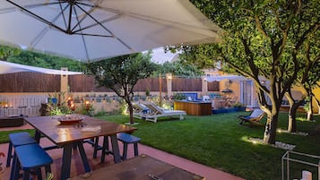Relax in a serene outdoor space surrounded by lush greenery and trees, featuring a patio with a table, benches, lounge chairs, and a cozy seating area.