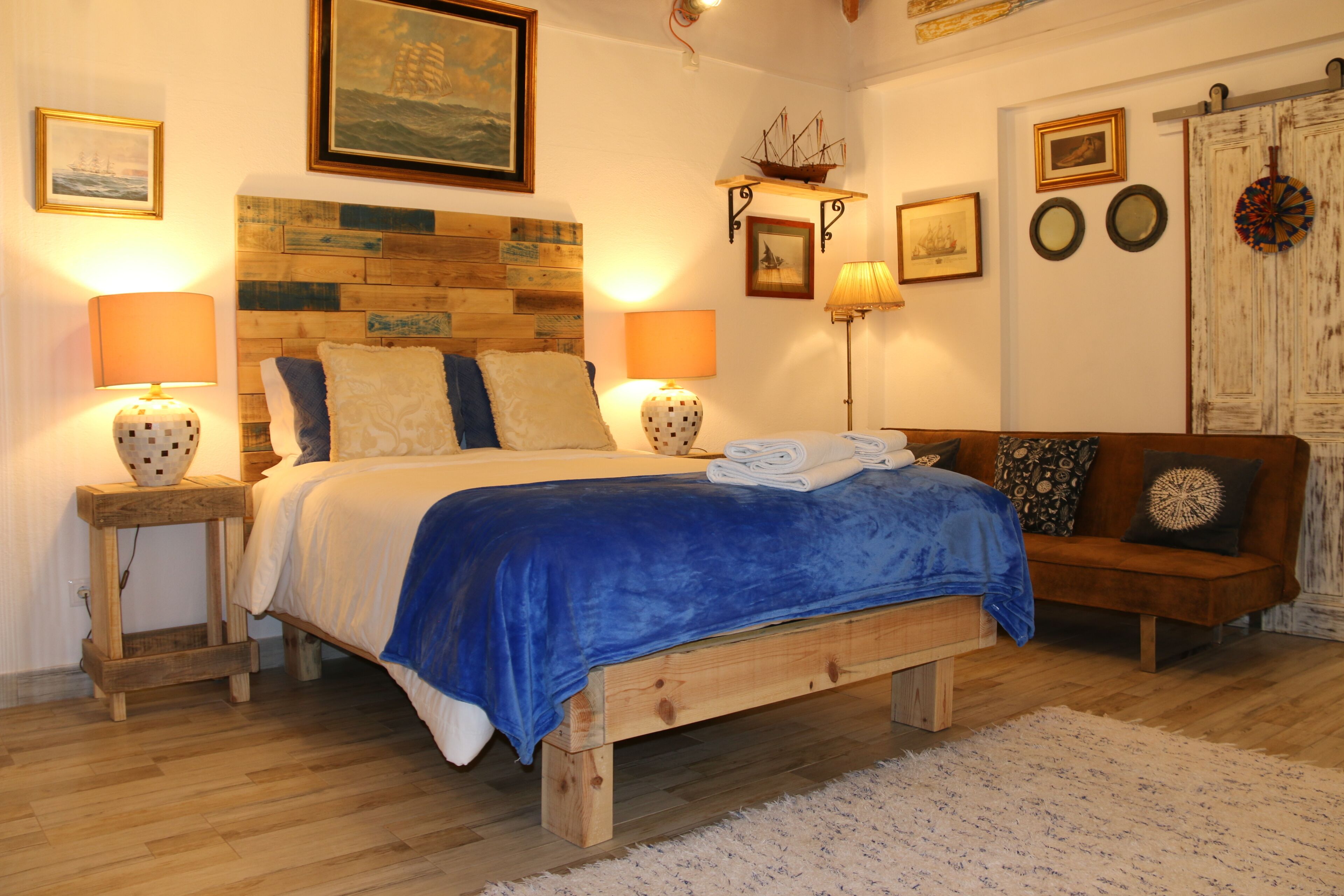 Ein Schlafzimmer mit einem hölzernen Kopfende, zwei Nachttischen mit Lampen, einem Bett mit blauer Decke, einer hölzernen Bank und einer rustikalen Tür.