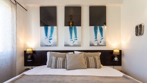 A neatly made bed with a fluffy blanket, two bedside lamps, and three abstract paintings on the wall above. - Geronimo Guest House Belém (Lisbon)